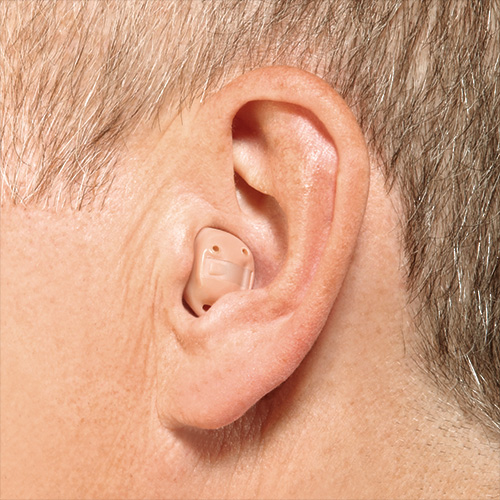 Apparecchio acustico endoauricolare color carne inserito nella conca dell'orecchio di un uomo con capelli brizzolati